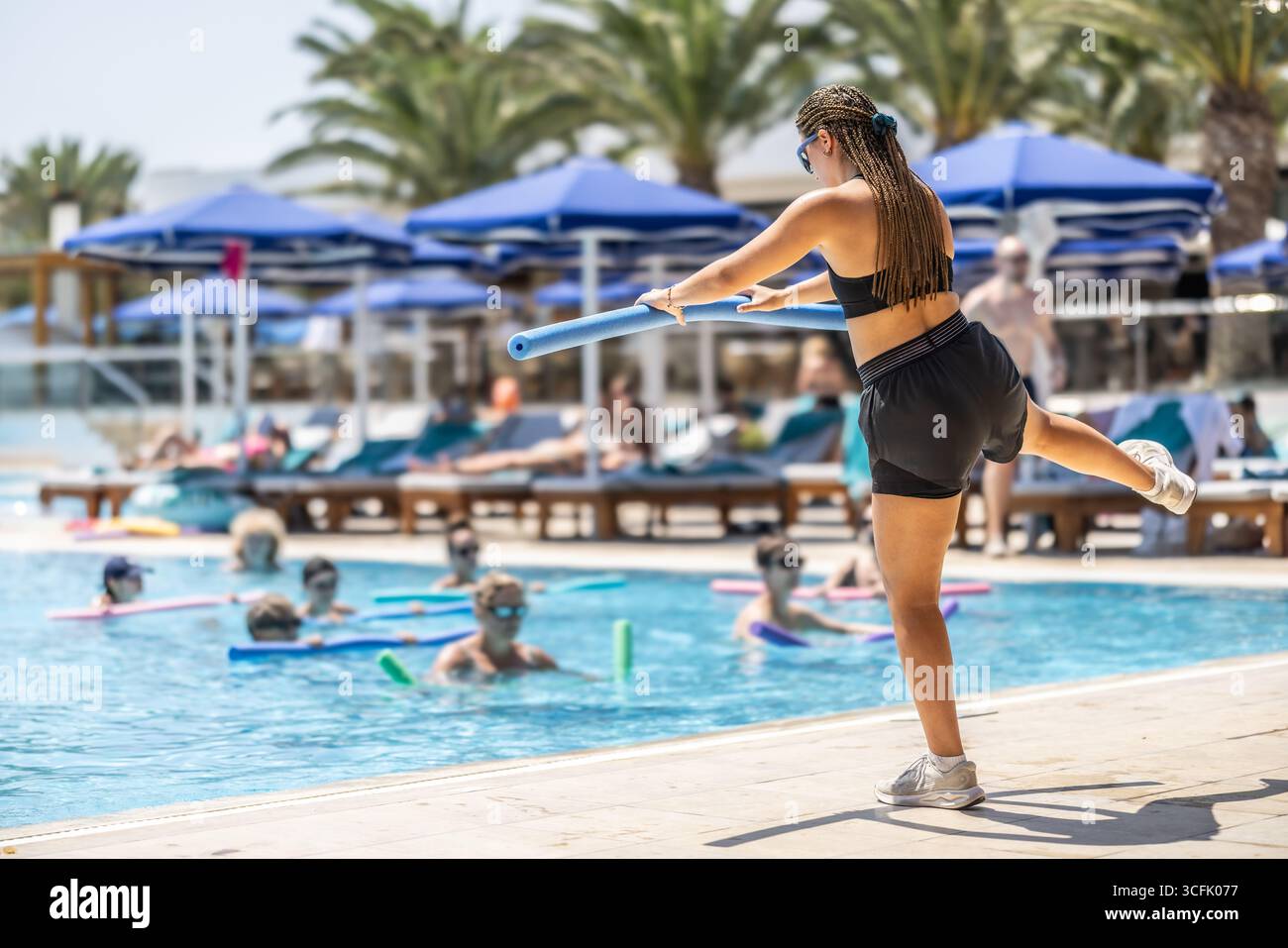 Eine junge weibliche Sportanimatorin macht Wassergymnastik für Menschen im Pool eines Hotelresorts. Stockfoto