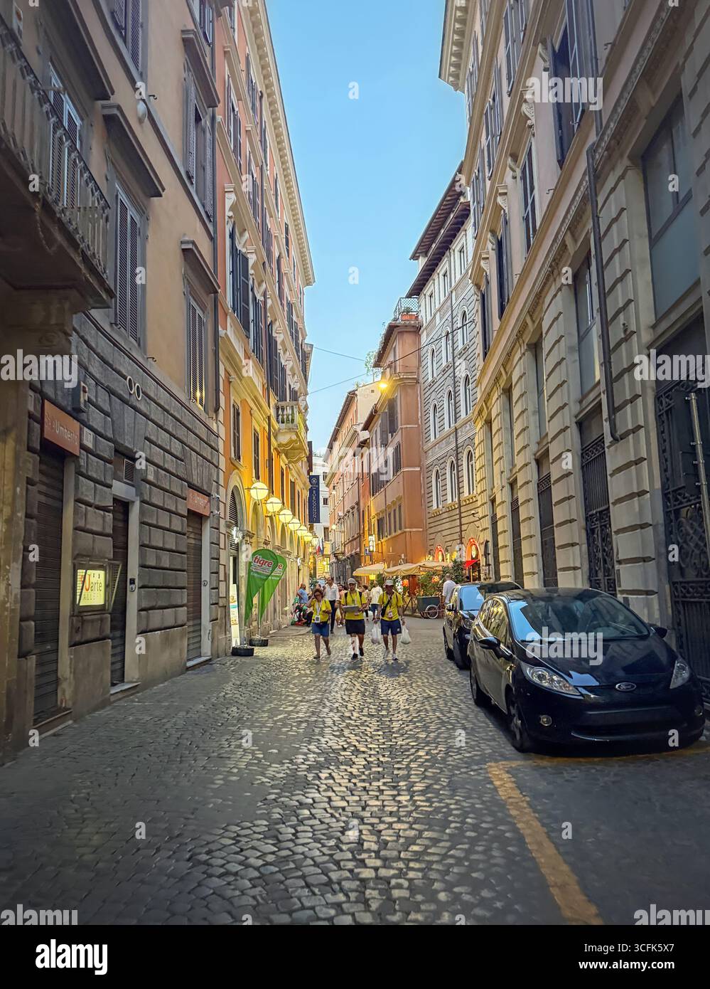 ROM, ITALIEN - 31. JULI 2025 Abendblick auf eine enge, kopfsteingepflasterte Straße in Rom, flankiert von hohen, historischen Gebäuden. Warme, einladende Atmosphäre mit Stockfoto