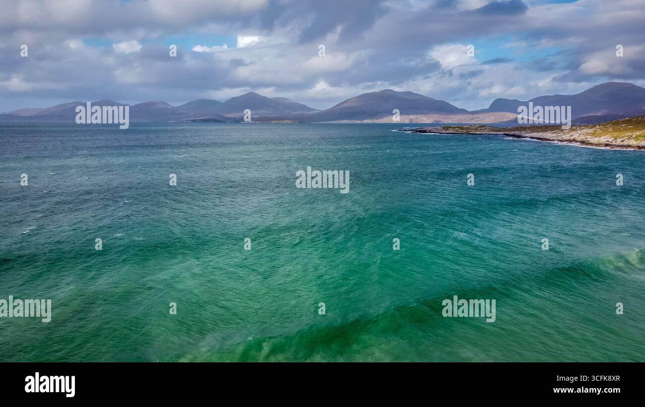 Drohnenblick auf das klare grüne Wasser entlang der Küste von Luskentyre mit entfernten Hügeln unter hellem Himmel Stockfoto