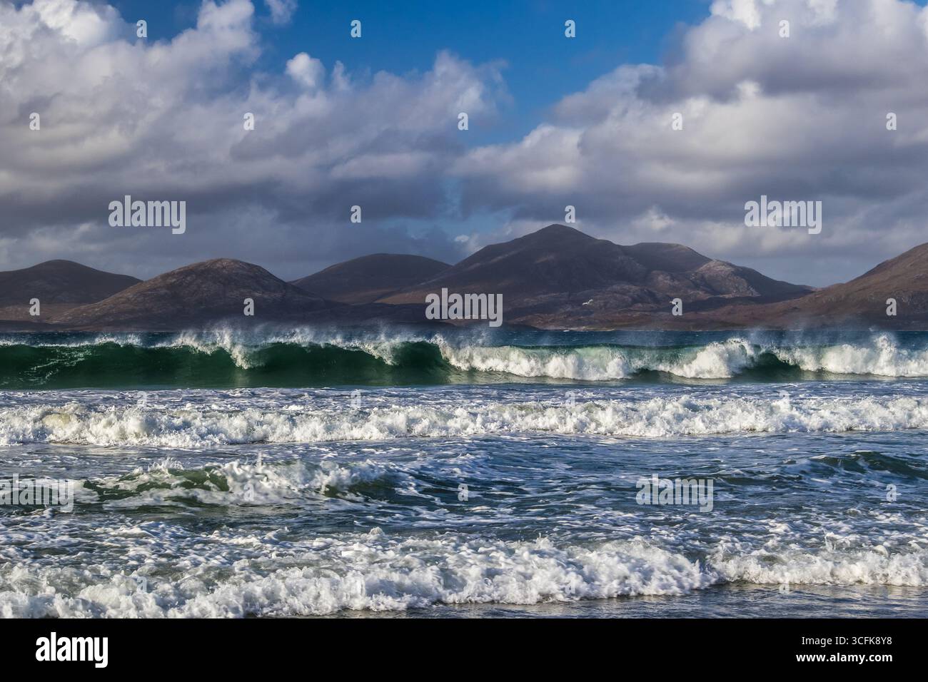 Dynamisches Surfen unter hellem Himmel am Strand von Luskentyre mit weit entfernten Bergen, die sich über das türkisfarbene Meer erheben Stockfoto
