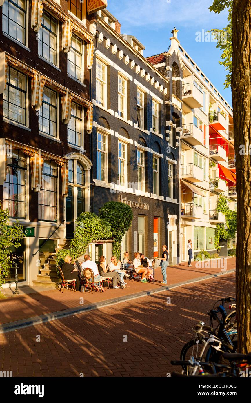 Amsterdamer Grachtenstraße mit Bäumen und Café-Terrasse im warmen Abendlicht, Niederlande Stockfoto