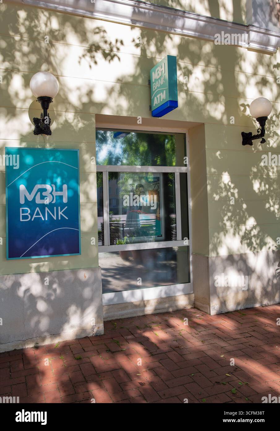 Nagykanizsa, Ungarn - 18. Mai 2025: Moderner Geldautomat der MBH Bank mit blauem Firmenschild, Glaseingang und traditionellen Straßenlaternen mit Stockfoto