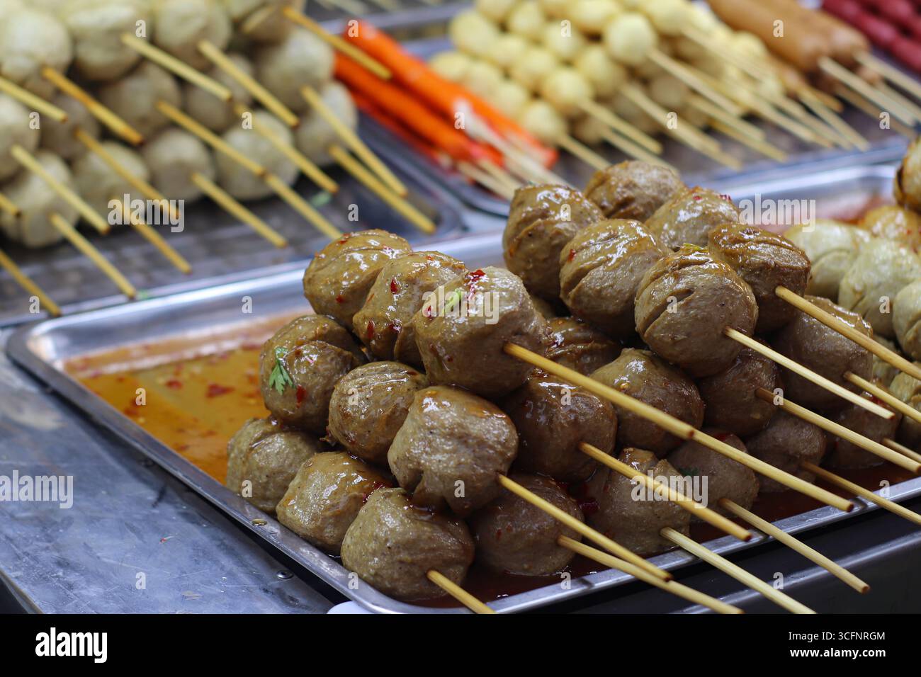 Rindfleischspieße mit glänzender süß-scharfer Sauce, garniert mit Kräutern und Chili an einem thailändischen Straßenmarkt. Stockfoto