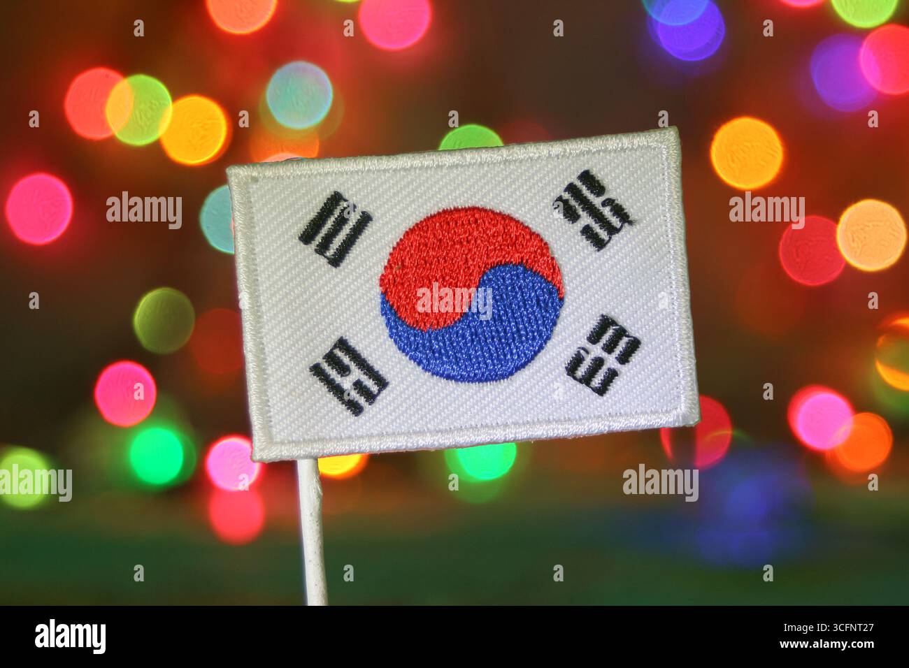 Die Stickerei mit der südkoreanischen Flagge mit einem Regenbogen-Bokeh-Hintergrund, der an ein Feuerwerk erinnert, ist perfekt für Neujahr, Weihnachten oder nationale Feiertage. Stockfoto