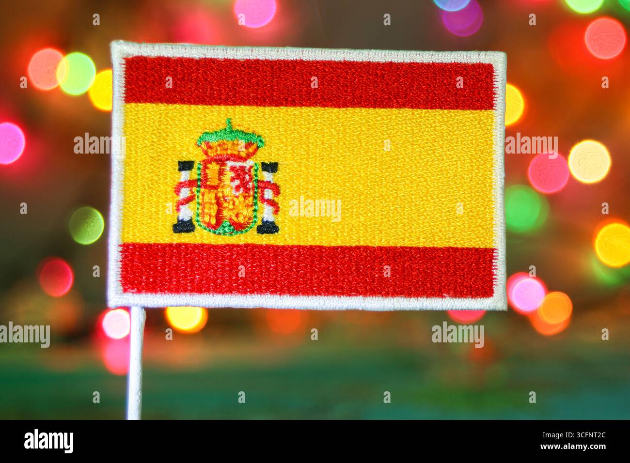 Die spanische Flaggenstickerei vor Regenbogenlichtern, die an ein Feuerwerk erinnern, ist perfekt für Neujahr, Weihnachten oder nationale Feiertage. Stockfoto