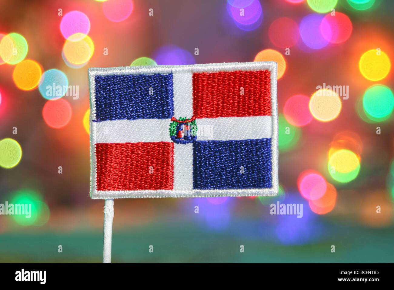 Gestickte Flagge der Dominikanischen Republik mit bunten Bokeh-Lichtern, festliche Feierstimmung, symbolisiert Nationalstolz und Urlaubsfreude. Stockfoto