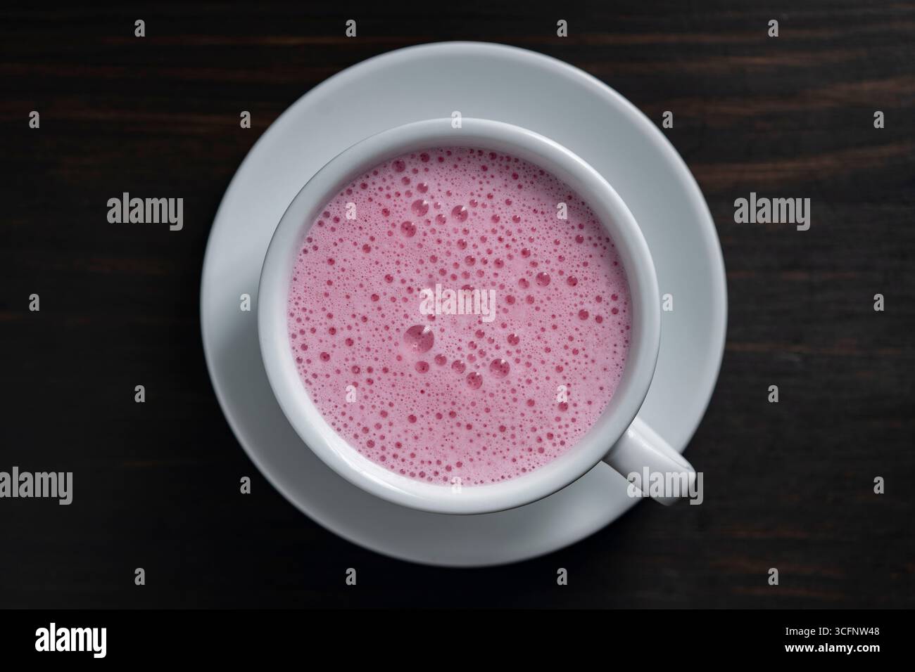 Rosa Matcha Latte mit Milch in weißer Tasse auf hölzernem Hintergrund, Nahaufnahme, Draufsicht. Trendiges Getränkekonzept Stockfoto