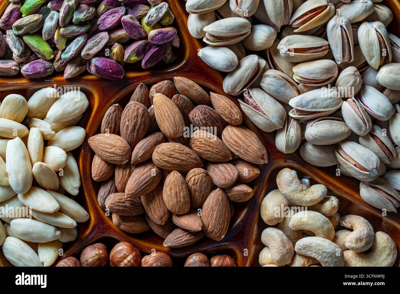 Nusssortiment in Keramikschale auf Hintergrund, Nahaufnahme, Draufsicht, Kopierraum. Cashew, Haselnüsse, Pistazien und Mandelnüsse zum Essen. Vegetarisch Stockfoto