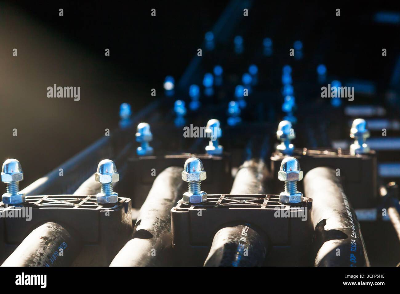 Nahaufnahme einer elektrischen Leitung von schweren, dicken Kabeln, die mit verschraubten Klemmen verlegt und geklemmt sind. Stockfoto