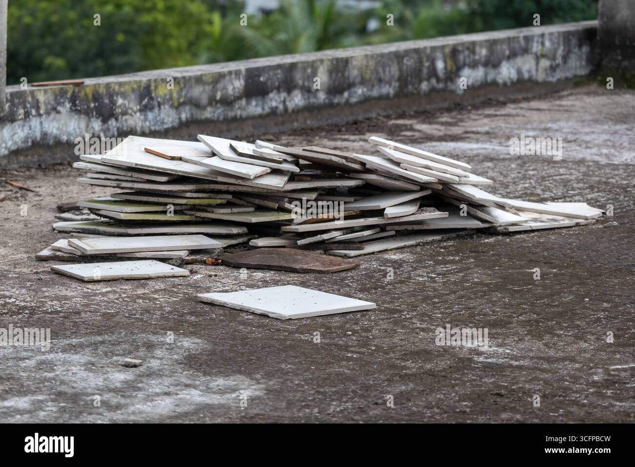 Stapel von entsorgten, verwitterten Bodenfliesen und Bruchstücken auf einer kiesigen Dachbetonoberfläche. Stockfoto