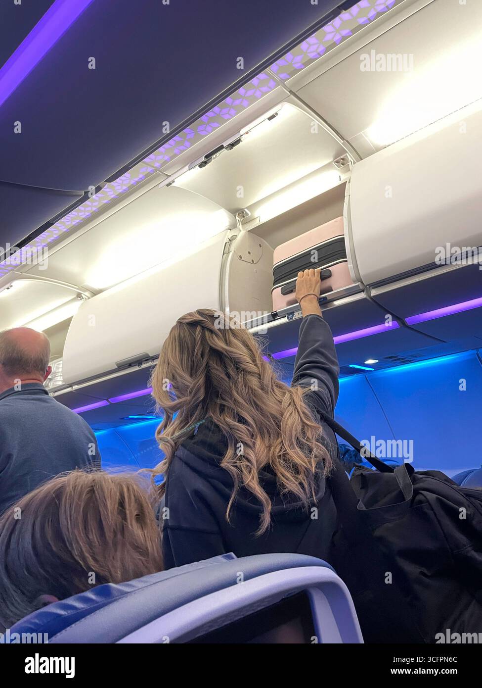 Eine junge Frau, die ihren riesigen Handgepäckkoffer bei Ankunft ihres Delta-Fluges im JFK-Flughafen, 2025, USA, aus dem Gepäckraum entfernt - Smartphone-aufgenommenes Stockfoto