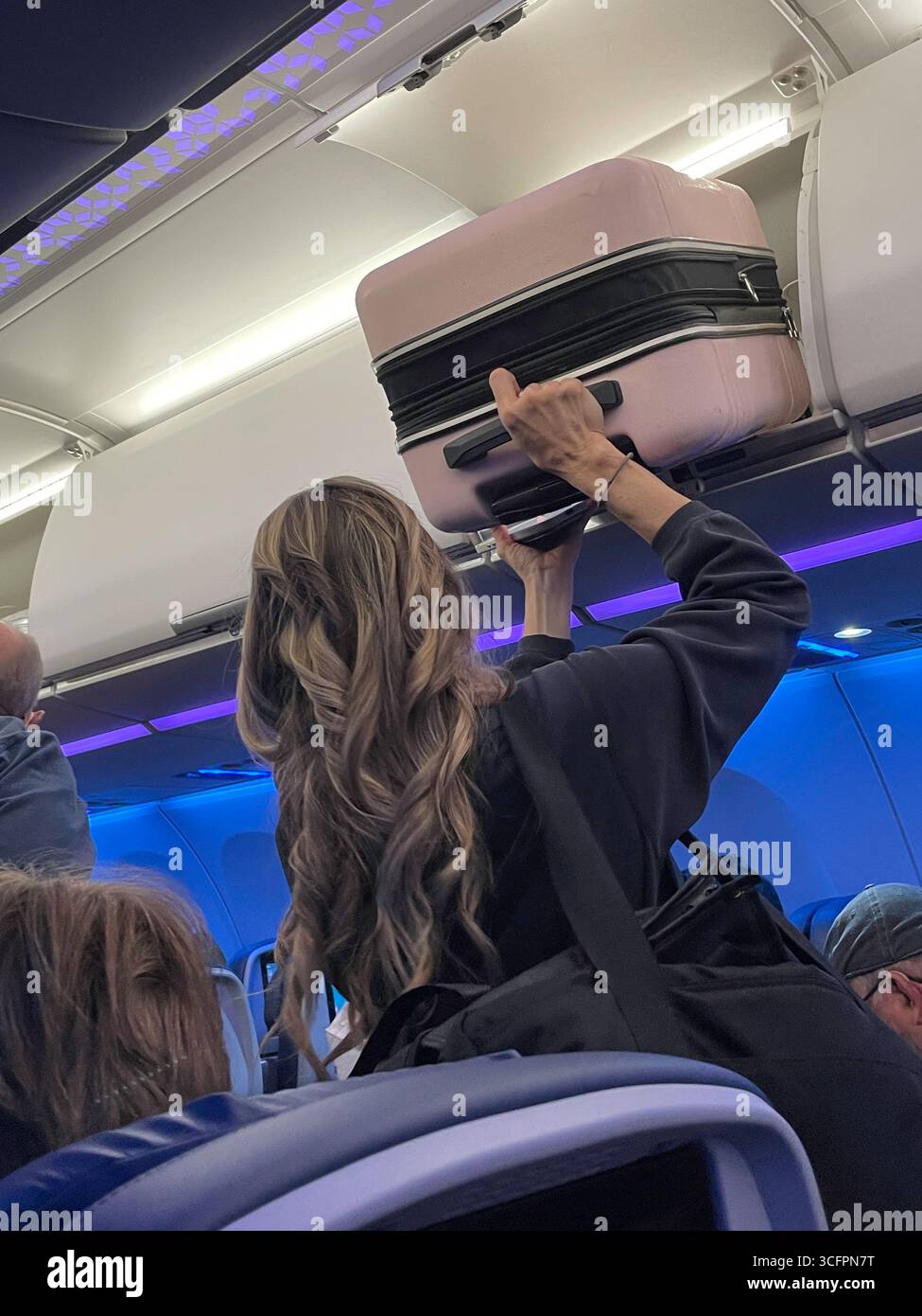 Eine junge Frau, die ihren riesigen Handgepäckkoffer bei Ankunft ihres Delta-Fluges im JFK-Flughafen, 2025, USA, aus dem Gepäckraum entfernt - Smartphone-aufgenommenes Stockfoto