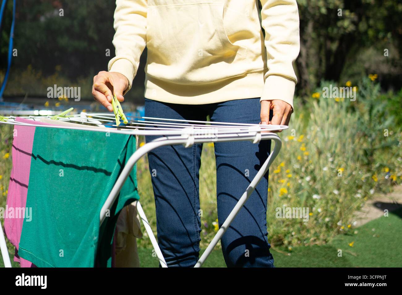 Frau hängt Wäsche an einer Wäscheleine in einem Garten und erledigt Haushaltsarbeiten an einem sonnigen Tag Stockfoto