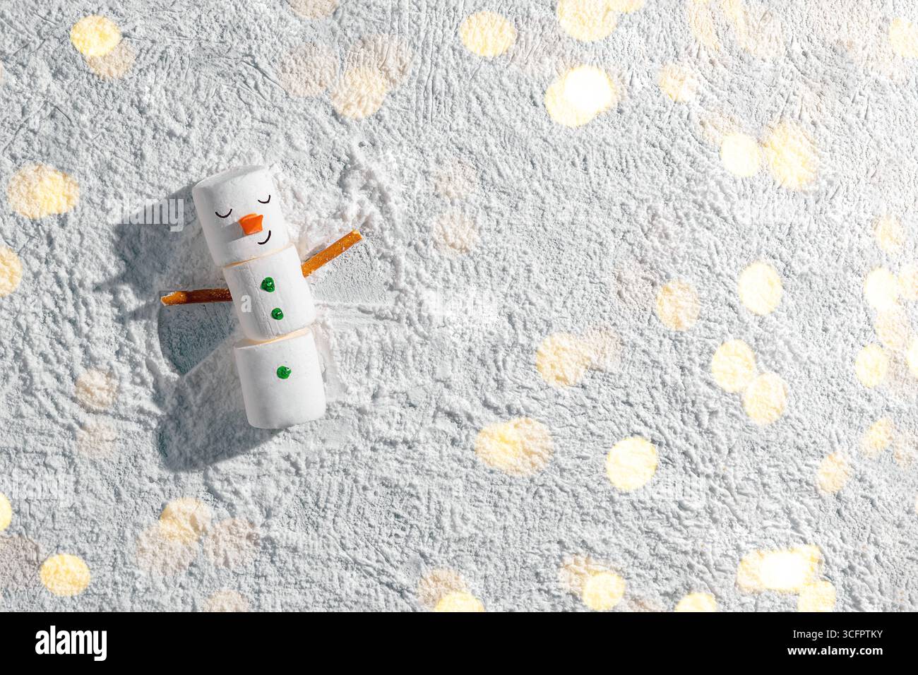 Lustiger Schneemann aus Marshmallow, der auf Schnee liegt und einen Schneeengel mit Brezel-Stabarmen kreiert, der den verspielten Geist der Winterferien und der festlichen ce einfängt Stockfoto