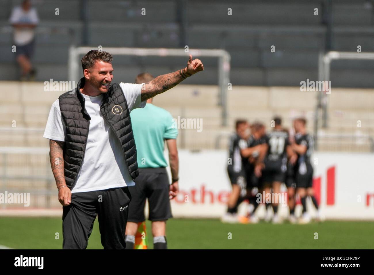 Freiburg Im Breisgau, Deutschland. August 2025. Pascal Reinhardt (SG Sonnenhof Gro?aspach, Trainer) nach dem 0:1 der mit Daumen hoch in Richtung Maximilian Reule (SG Sonnenhof Gro?aspach, 1) zeigt und sich freut und im Hintergrund sieht man die Mannschaft bei Torjubel Regionalliga S?dwest, SC Freiburg U23 vs SG Sonnenhof Gro?aspach, Dreisamtstadion, 24.08.2025 DFB/DFL-VORSCHRIFTEN VERBIETEN JEDE VERWENDUNG VON FOTOGRAFIEN ALS BILDSEQUENZEN und/Alamy News Stockfoto