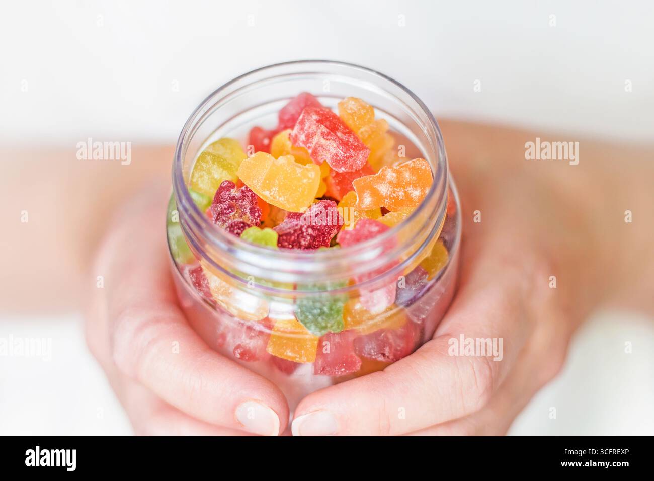 Weibliche Hände halten ein Glas Gummibären nahe. Süßigkeiten für Kinder. Nahaufnahme Stockfoto