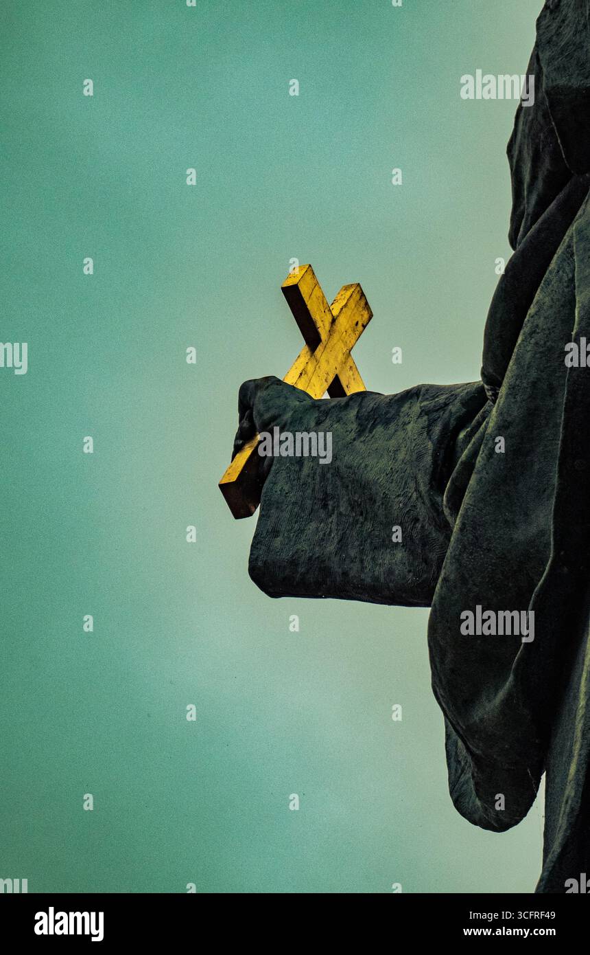 Nahaufnahme einer Hand, die ein goldenes Kreuz vor einem weichen grünen Hintergrund hält, St. Gerard Sagredo Statue, Budapest Stockfoto