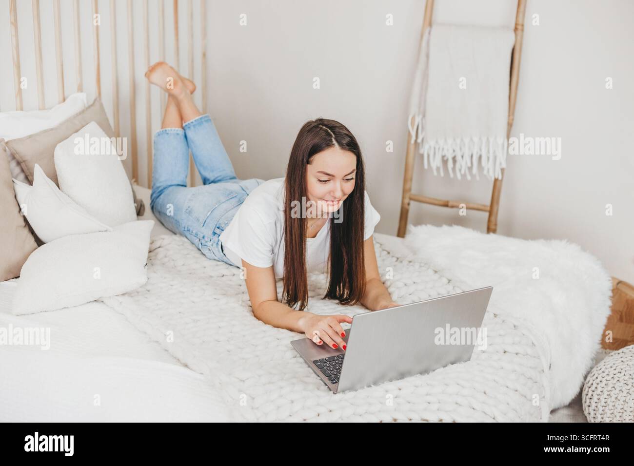 Die Werbemanagerin für Mädchen arbeitet zu Hause mit einem Laptop, der auf einem weißen Bett von oben liegt. Moderner Beruf Stockfoto
