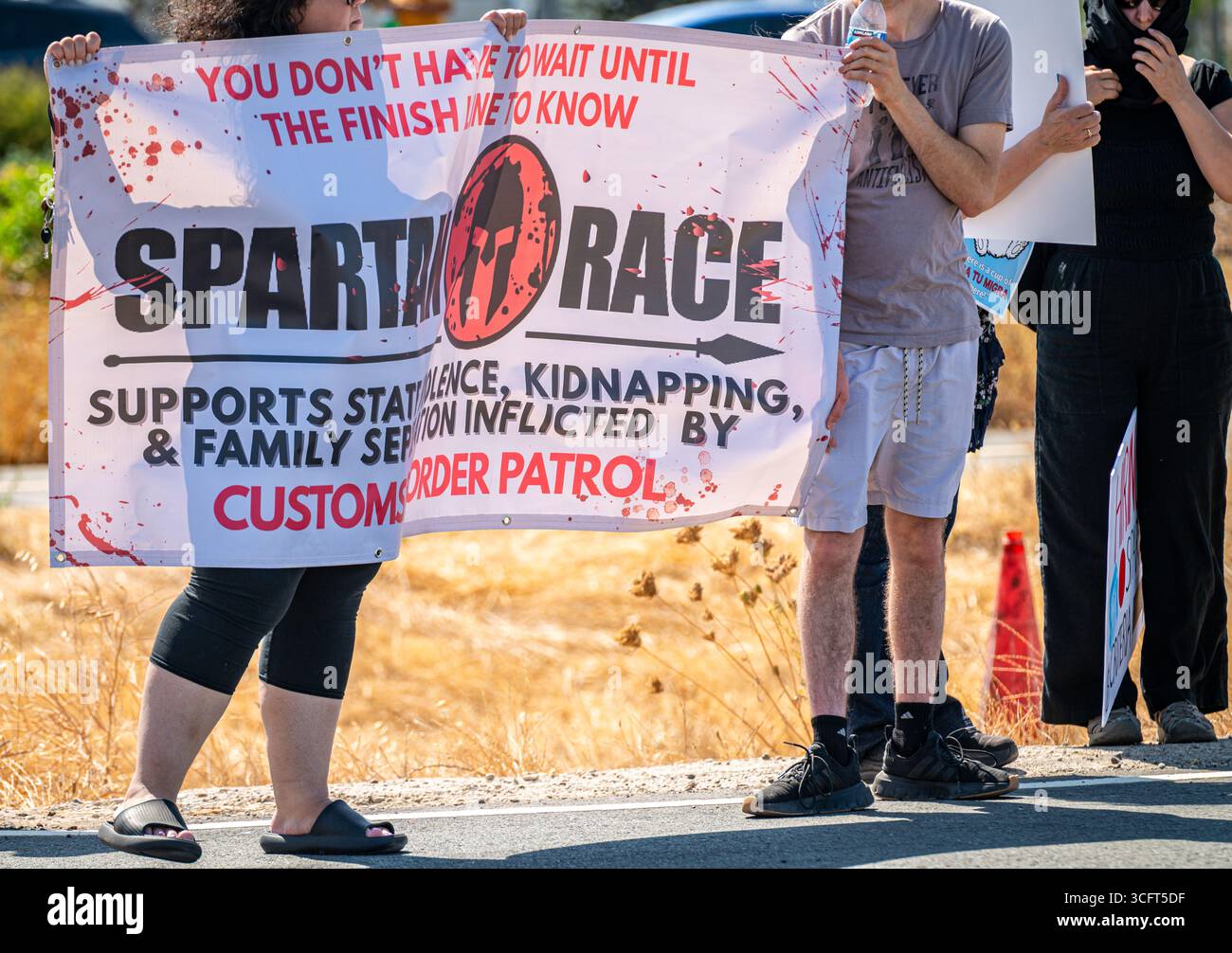 Die Demonstranten halten ein Informationsbanner in der Nähe eines von der Zoll- und Grenzkontrolle (CBP) gesponserten Spartan Race-Events, bei dem ICE rekrutiert wird. Stockfoto Die Demonstranten halten ein Informationsbanner in der Nähe eines von der Zoll- und Grenzkontrolle (CBP) gesponserten Spartan Race-Events, bei dem ICE rekrutiert wird. Stockfoto
