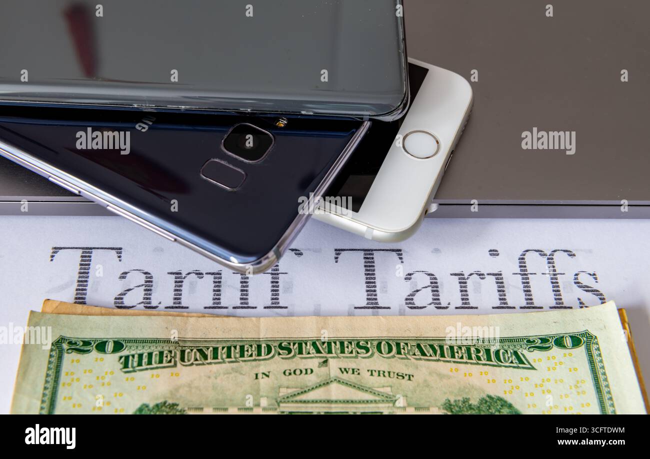 Mobiltelefone, Laptop-Computer und ein Stapel US-Dollar-Scheine auf weißem Hintergrund mit den gedruckten Worten Tarif, Tarife. Ein US-Zollsteuerkonzept. Stockfoto