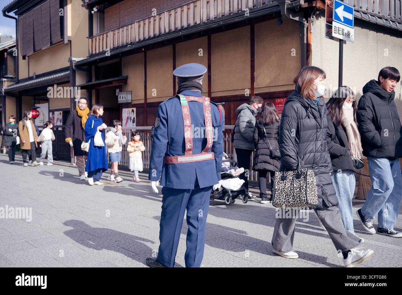 Uniformierter Offizier beobachtet, wie die Menschen im Winter auf einer sonnigen Straße in Kyoto spazieren Stockfoto