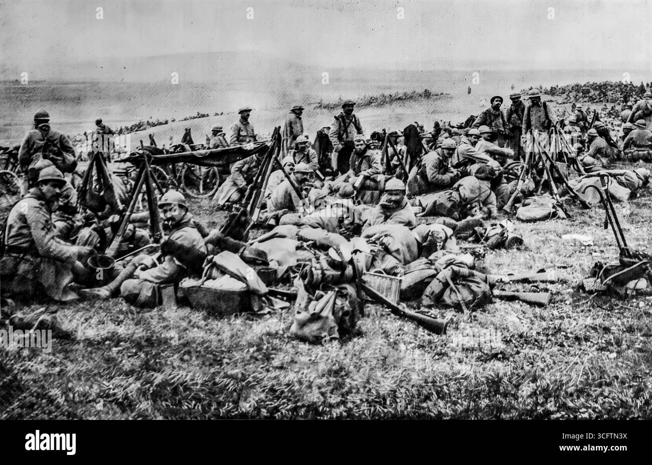 Foto aus L’Illustration (1916), das französische Soldaten zeigt, die während des Ersten Weltkriegs hinter der Verdun-Front ruhten und sich in Gruppen versammeln, wobei Gewehre auf dem Feld gestapelt sind. Die Szene zeigt die Erschöpfung der Soldaten während der Schlacht von Verdun, einer der längsten und blutigsten Schlachten des Krieges, während sie einen seltenen Moment der Ruhe abseits der Front festnimmt. Stockfoto