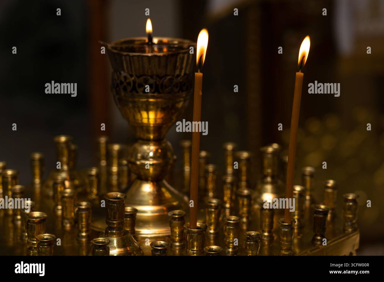 Helle Flammen von zwei Kerzen und eine dekorative Öllampe schaffen ein warmes Ambiente an einem friedlichen Ort der Anbetung. Der goldene Farbton verleiht dem Ev Stockfoto