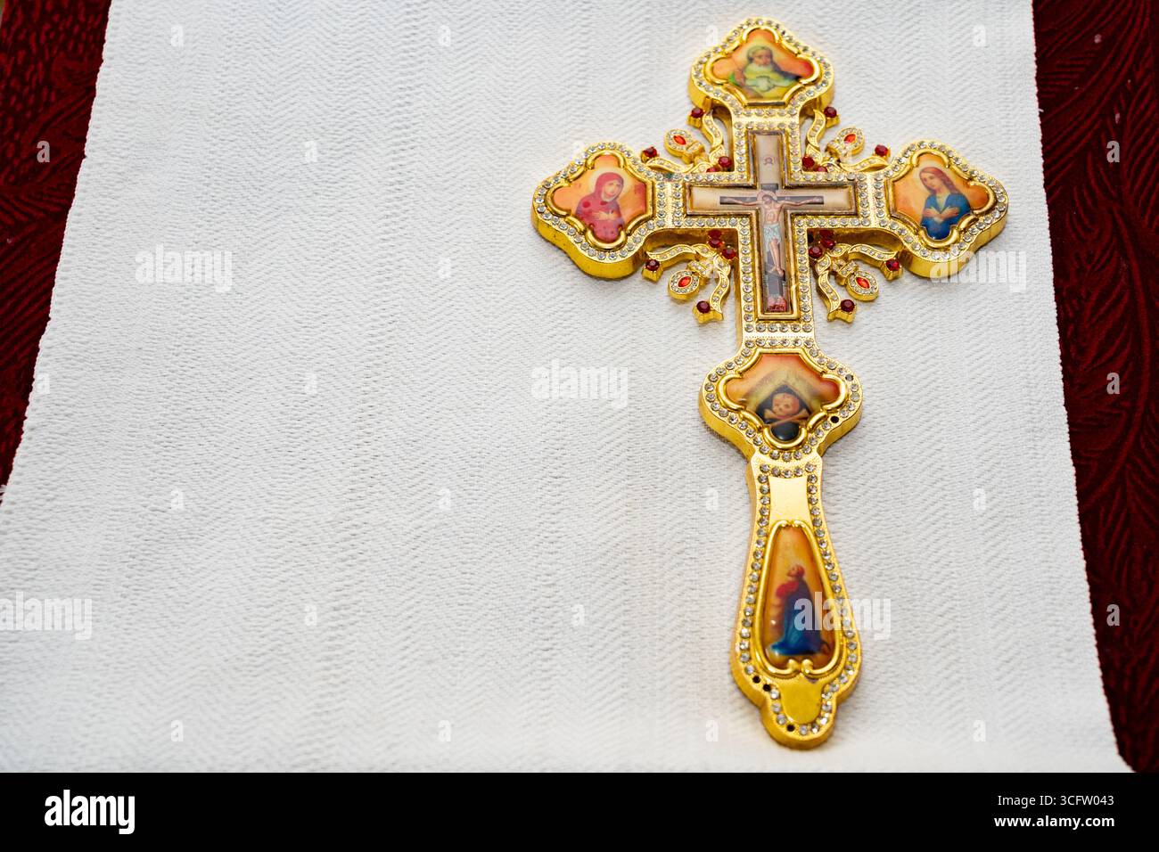 Das komplizierte goldene Kreuz mit lebendigen Darstellungen religiöser Figuren ist auf einem weichen weißen Leinen platziert. Das dekorative Design sorgt für einen Hauch von Revers Stockfoto
