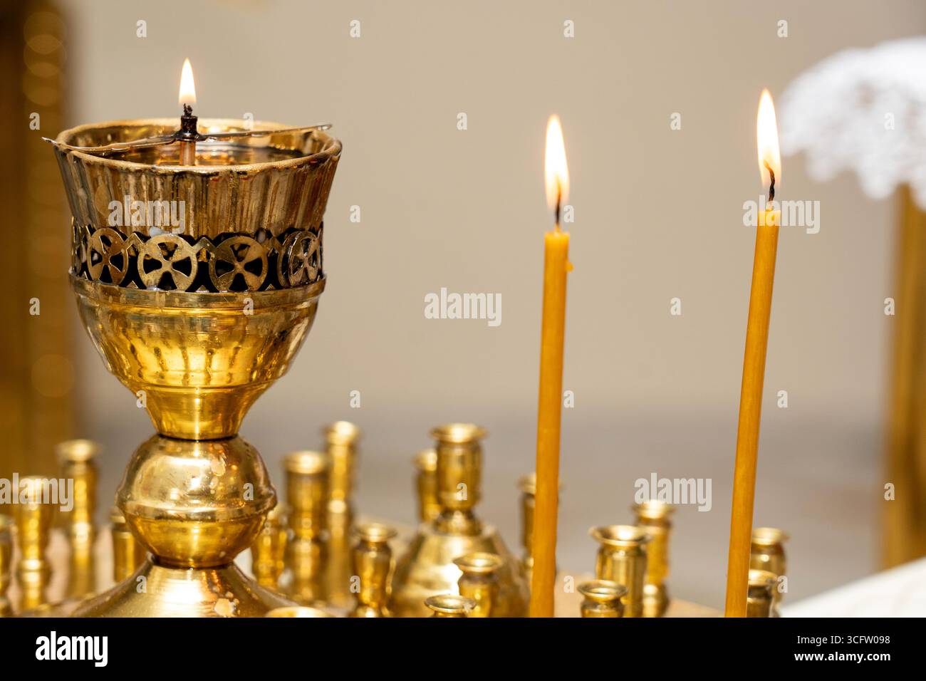 Ein wunderschön gefertigter goldener Kerzenständer steht mitten in einem ruhigen Raum, umgeben von leuchtenden Kerzen. Das warme Flackern der Flammen Stockfoto