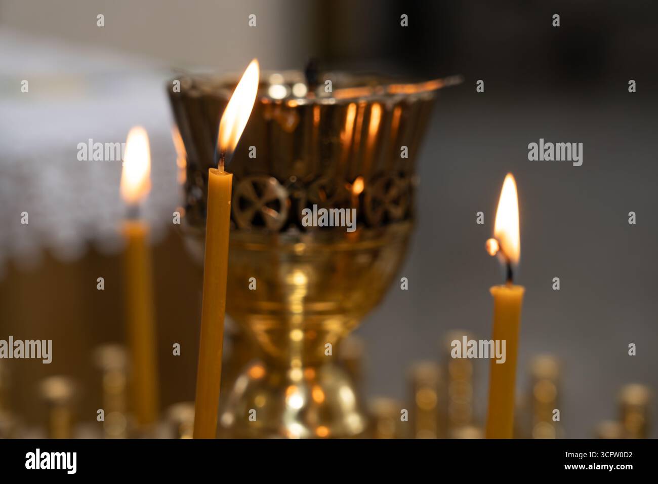 Goldener Kerzenhalter mit komplizierten Designs hält flackernde Kerzen und strahlt während einer Zusammenkunft ein warmes Leuchten in einer ruhigen spirituellen Atmosphäre aus. Stockfoto