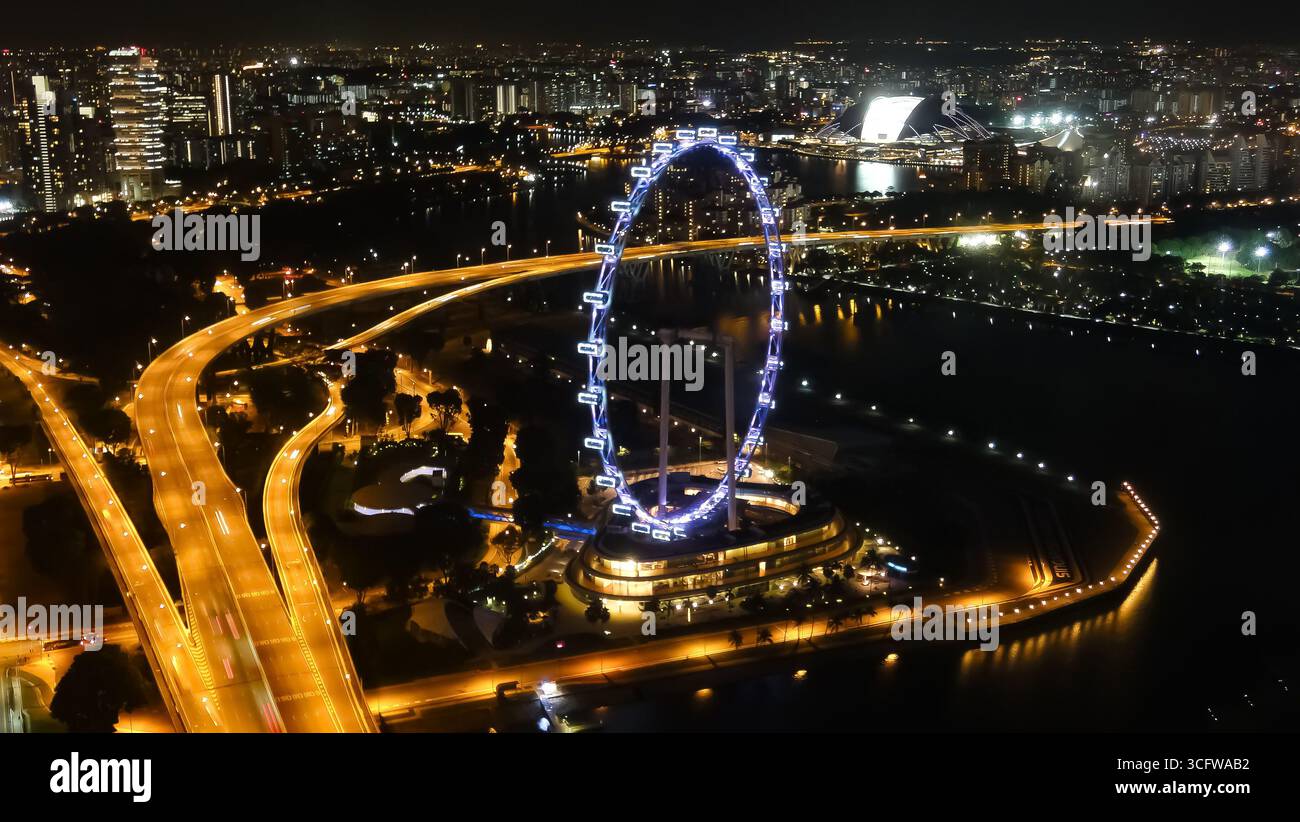 Das Singapore Flyer Ferris Wheel, ein bedeutendes Wahrzeichen, leuchtet nachts vor der Kulisse der Stadt hell. Stockfoto