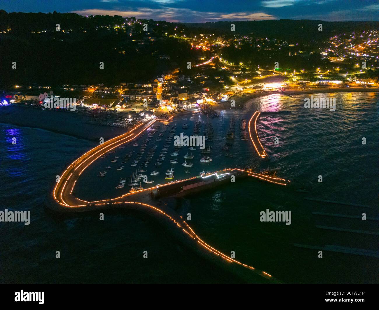 Lyme Regis, Dorset, Großbritannien. August 2025. Aus der Vogelperspektive der Candles on the Cobb Illumination im Badeort Lyme Regis in Dorset. Rund 5000 Kerzen wurden entlang der historischen Hafenmauern von Cobb angezündet, um an die Lieben zu erinnern, die von Tausenden von Zuschauern im Lister Garden und am Meer beobachtet wurden. Das gesammelte Geld wird aufgeteilt auf lokale gute Zwecke, Prostate Cancer UK und Macmillan Cancer Support. Bildnachweis: Graham Hunt/Alamy Live News Stockfoto
