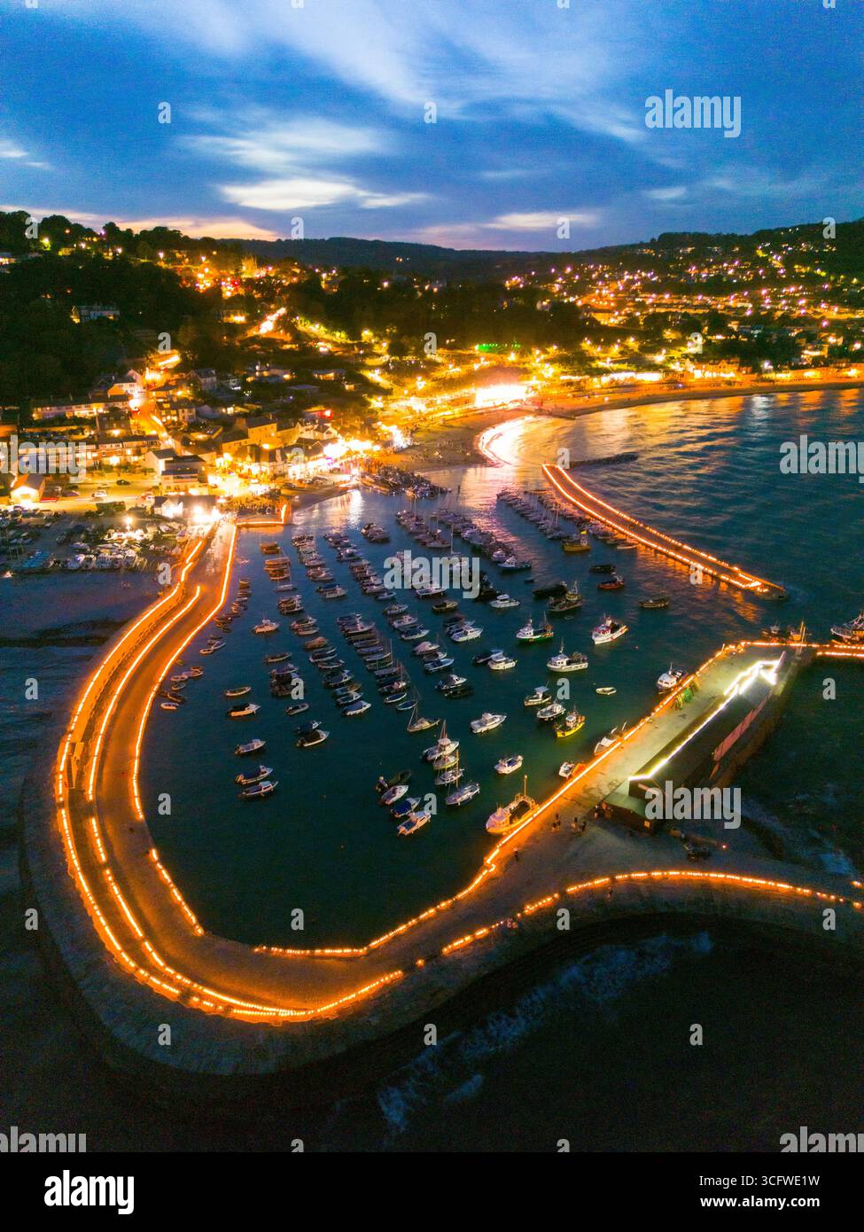 Lyme Regis, Dorset, Großbritannien. August 2025. Aus der Vogelperspektive der Candles on the Cobb Illumination im Badeort Lyme Regis in Dorset. Rund 5000 Kerzen wurden entlang der historischen Hafenmauern von Cobb angezündet, um an die Lieben zu erinnern, die von Tausenden von Zuschauern im Lister Garden und am Meer beobachtet wurden. Das gesammelte Geld wird aufgeteilt auf lokale gute Zwecke, Prostate Cancer UK und Macmillan Cancer Support. Bildnachweis: Graham Hunt/Alamy Live News Stockfoto
