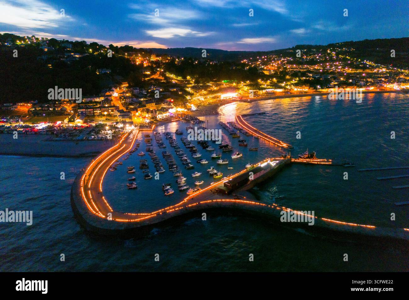 Lyme Regis, Dorset, Großbritannien. August 2025. Aus der Vogelperspektive der Candles on the Cobb Illumination im Badeort Lyme Regis in Dorset. Rund 5000 Kerzen wurden entlang der historischen Hafenmauern von Cobb angezündet, um an die Lieben zu erinnern, die von Tausenden von Zuschauern im Lister Garden und am Meer beobachtet wurden. Das gesammelte Geld wird aufgeteilt auf lokale gute Zwecke, Prostate Cancer UK und Macmillan Cancer Support. Bildnachweis: Graham Hunt/Alamy Live News Stockfoto