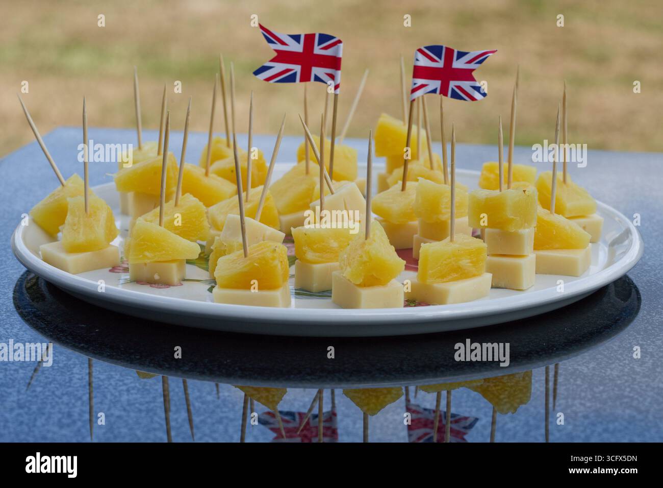 Käse- und Ananasstücke auf hölzernen Cocktailstangen. Zwei Gewerkschaftsflaggen auf dem Bild. Einfaches britisches Partyessen. Stockfoto