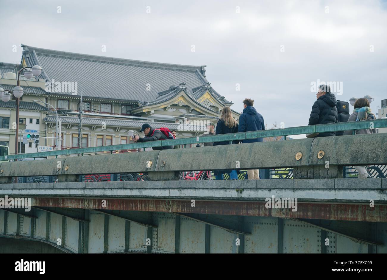 Kyoto-Brücke mit dem historischen Minamiza-Theater im Hintergrund, während sich ein Mann über das Geländer beugt, um ein Foto zu machen Stockfoto