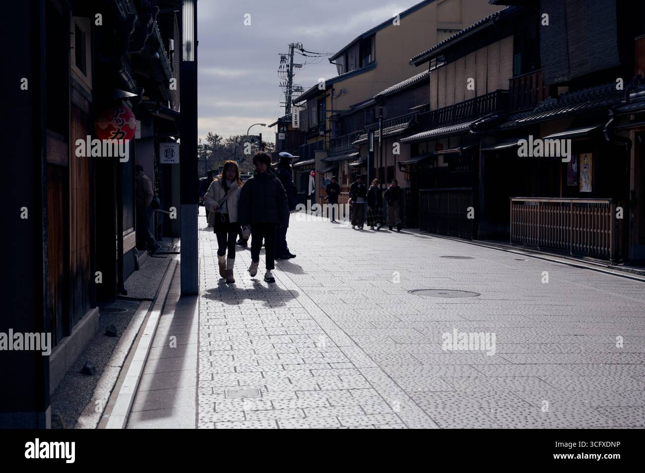 Silhouetten entlang einer traditionellen Straße in Kyoto, eingerahmt von historischen Machiya-Häusern aus Holz unter einem stimmungsvollen Winterhimmel Stockfoto