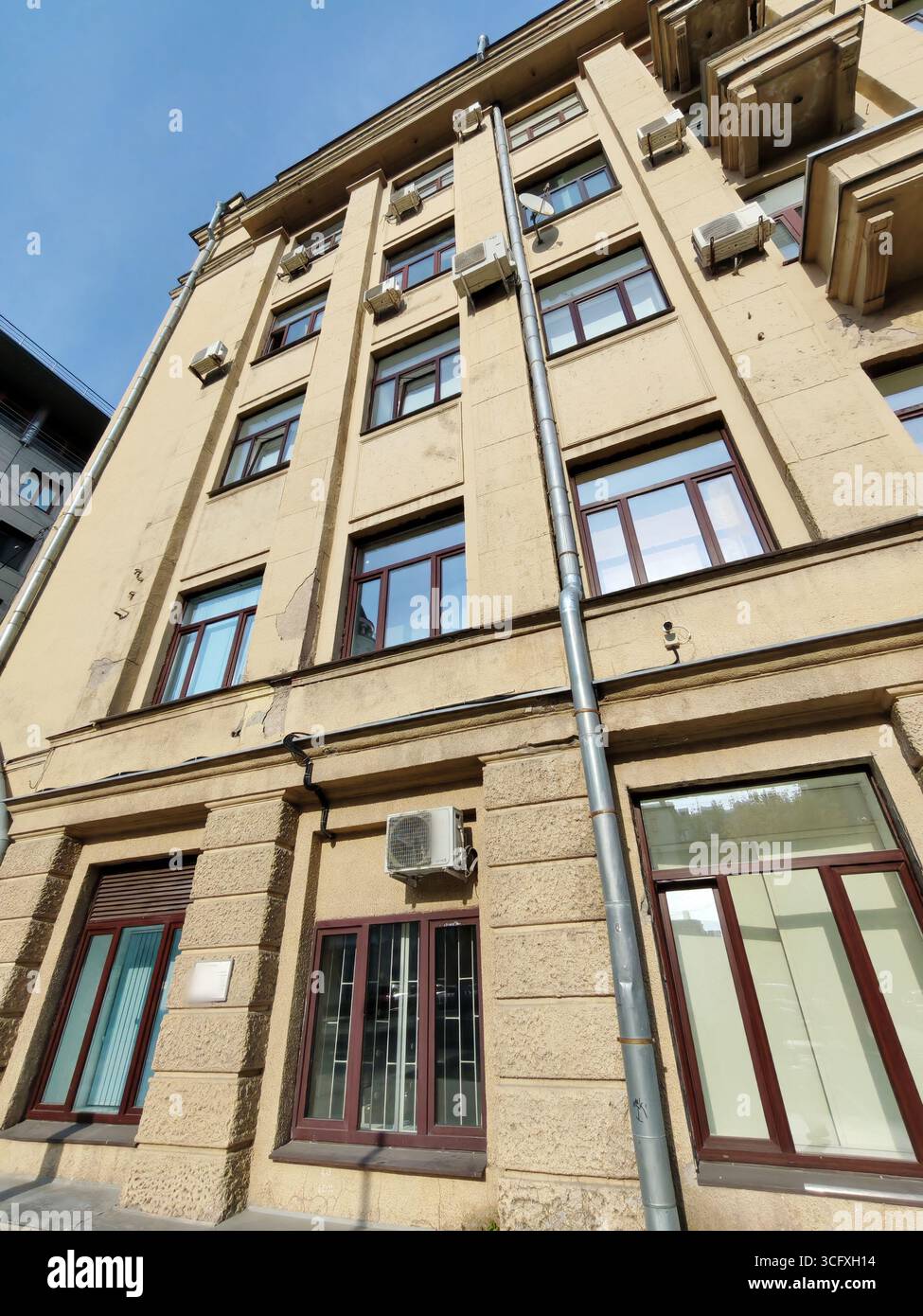 Eine mehrstöckige beigefarbene Fassade mit Balkonen, rechteckigen Fenstern und Gebrauchselementen wie Abflussrohren und Klimaanlagen. Das Foto spiegelt den wider Stockfoto