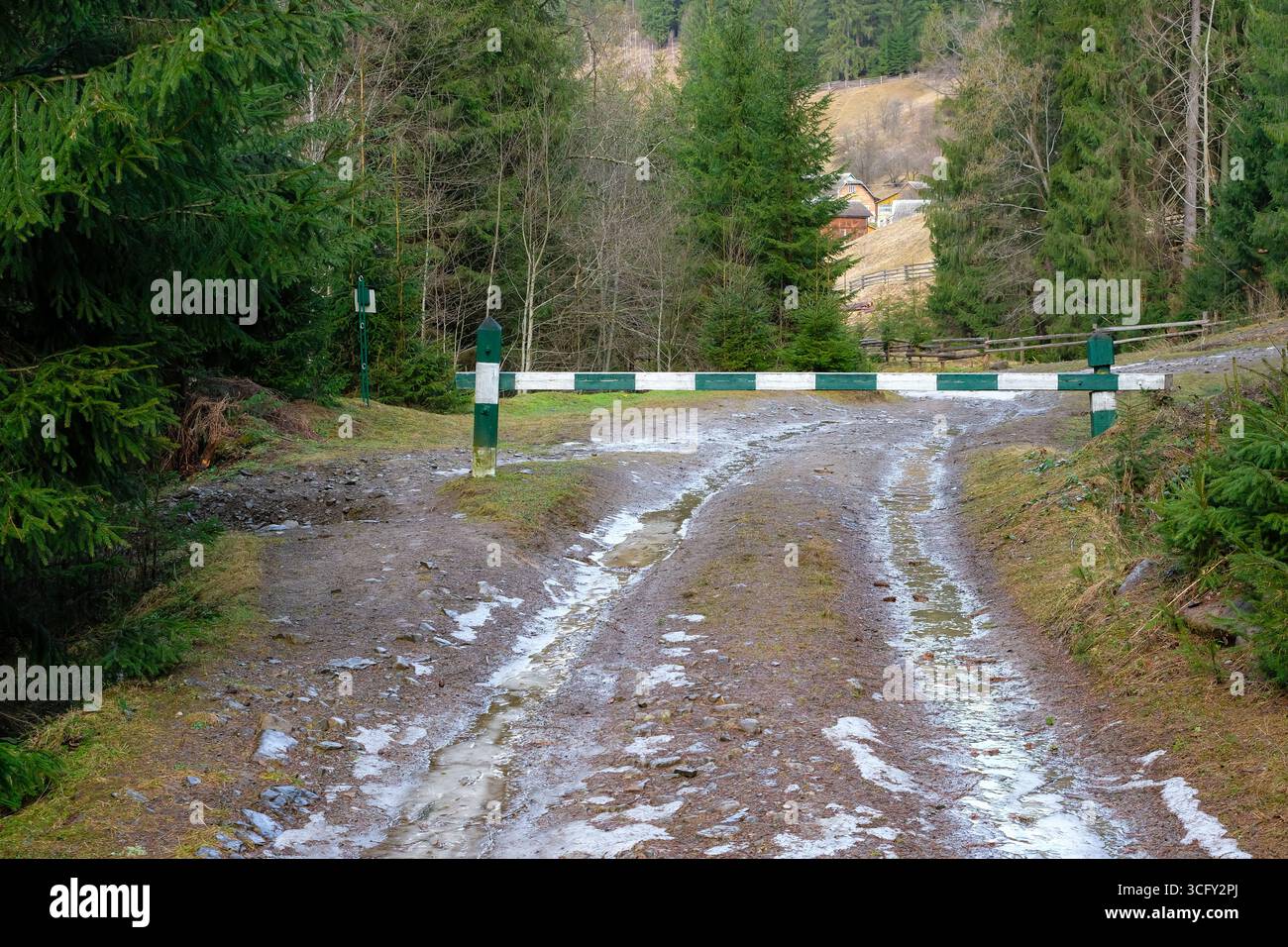 Blick von einem Fichtenwald zu einem Bergdorf durch eine ökologische Barriere auf einer Schotterstraße. Begrenzen Sie den Zugang zum Fahrzeug in einem Nationalpark. Stockfoto