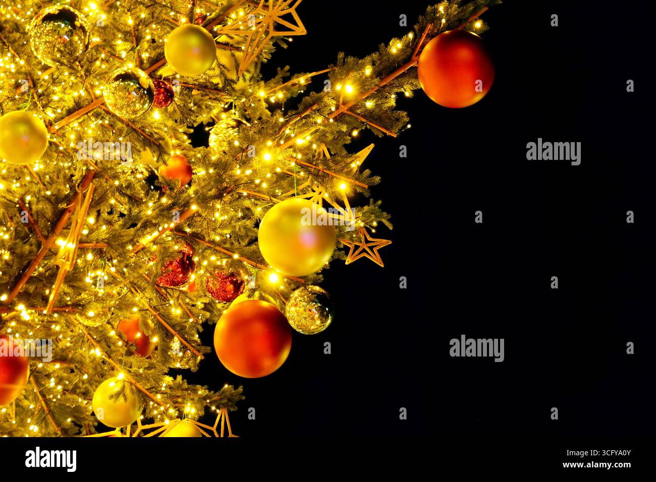 Weihnachtsbaumzweige mit warmen Lichtern, roten und goldenen Kugeln und Sternverzierungen auf schwarzem Hintergrund. Festliche Winterdekoration der Saison Stockfoto