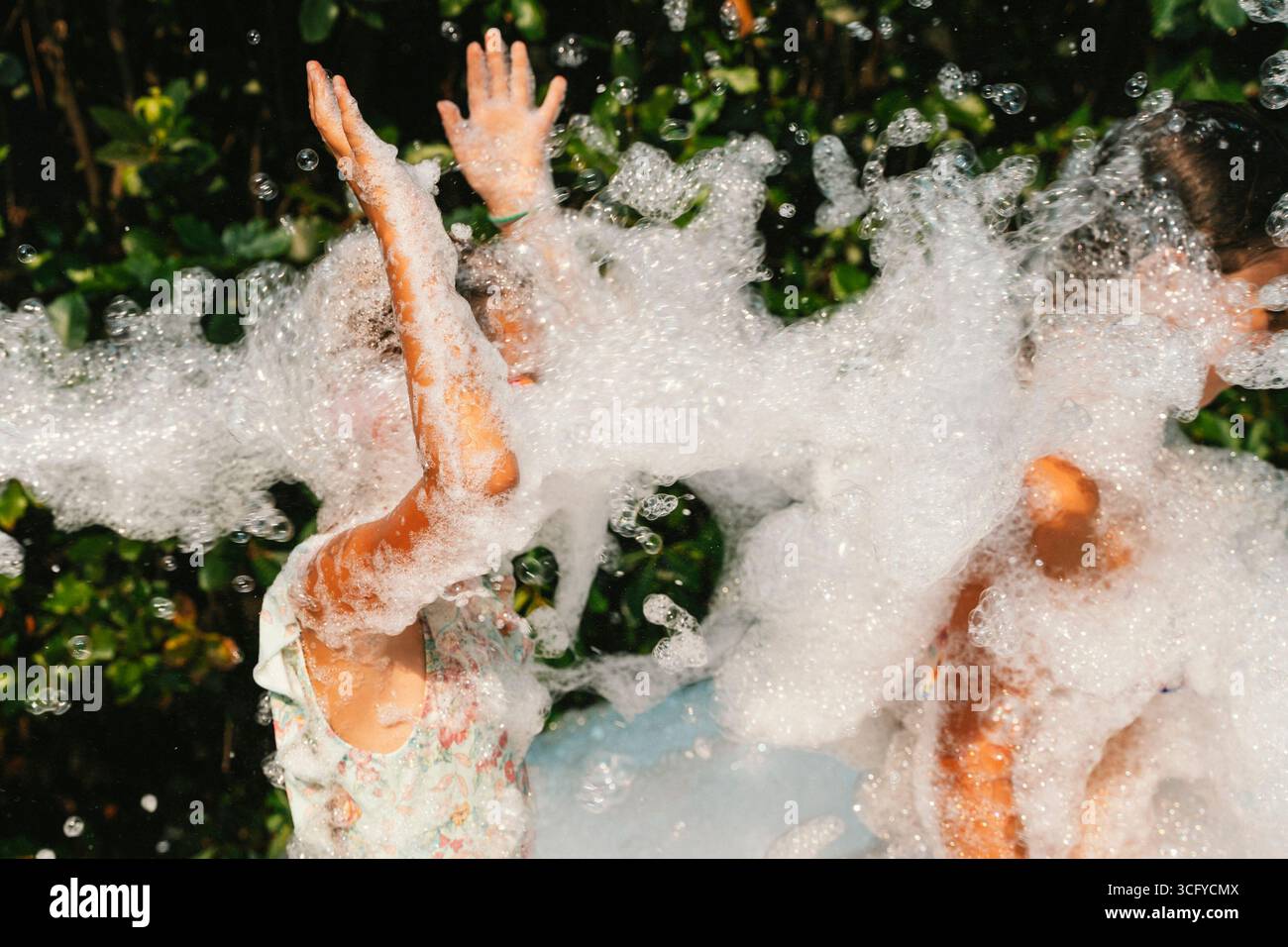 Kinder erfreuen sich an einem sorgenfreien Nachmittag, umgeben von Blasen. Ihre Gesichter drücken pure Freude und Spannung aus, wenn sie draußen spielen. Das Bild wird erfasst Stockfoto