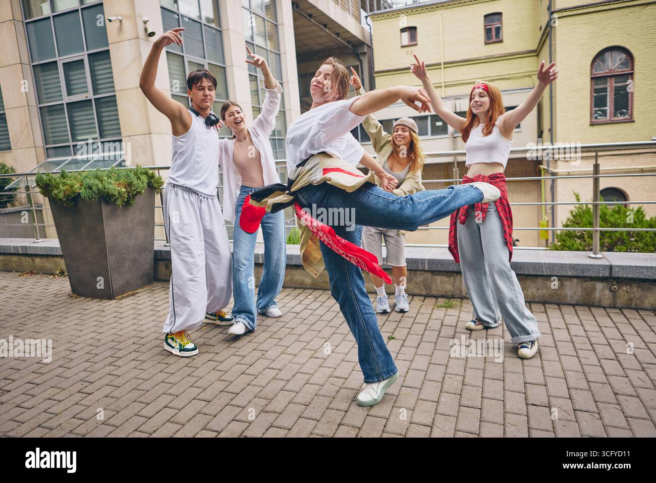 Tänzerin tritt vor Freude das Bein, während Freunde sich mit Lachen und Stil umgeben Stockfoto
