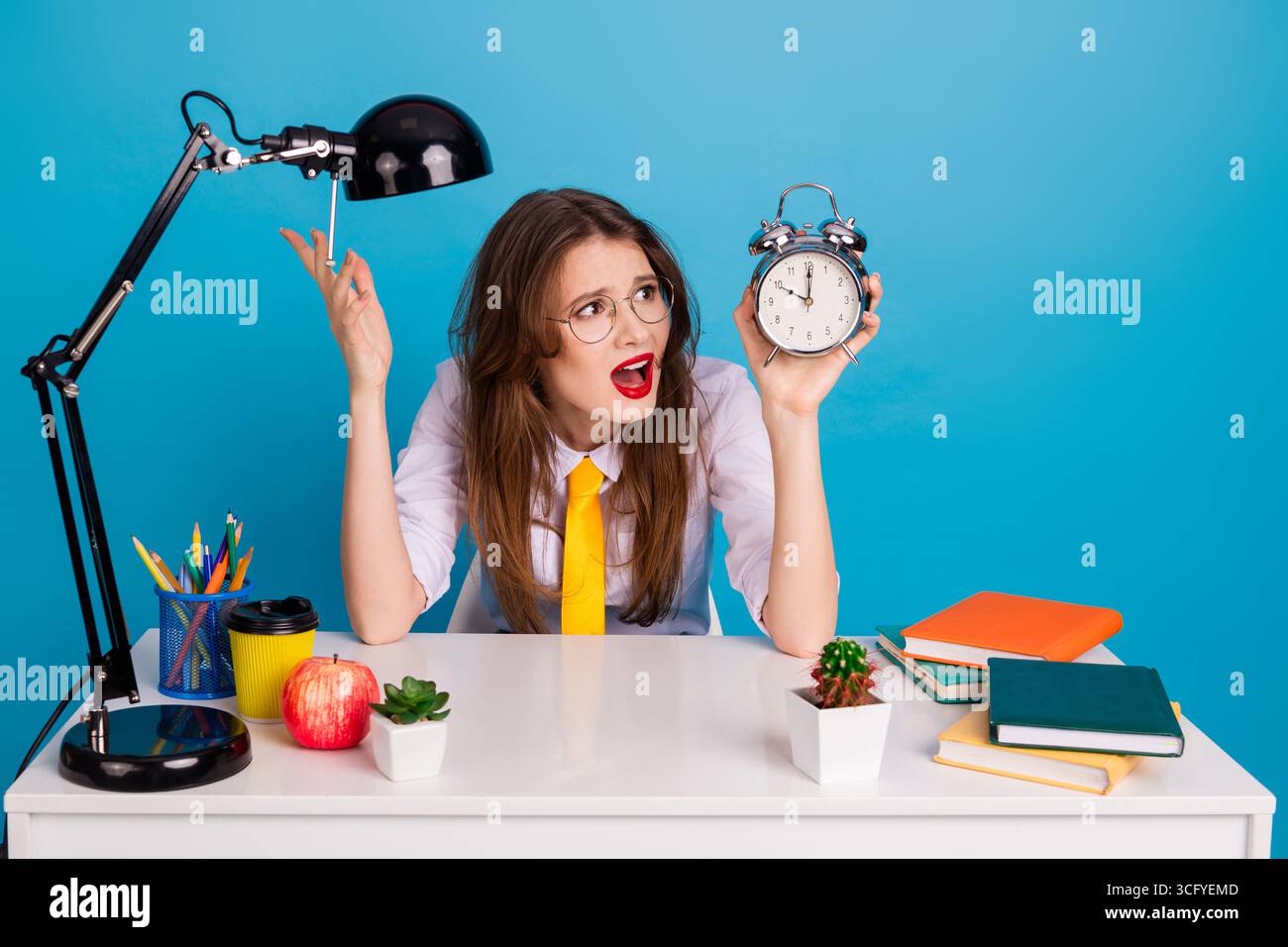 Frustrierter Student mit Wecker in farbenfroher Studieneinrichtung vor blauem Hintergrund Stockfoto