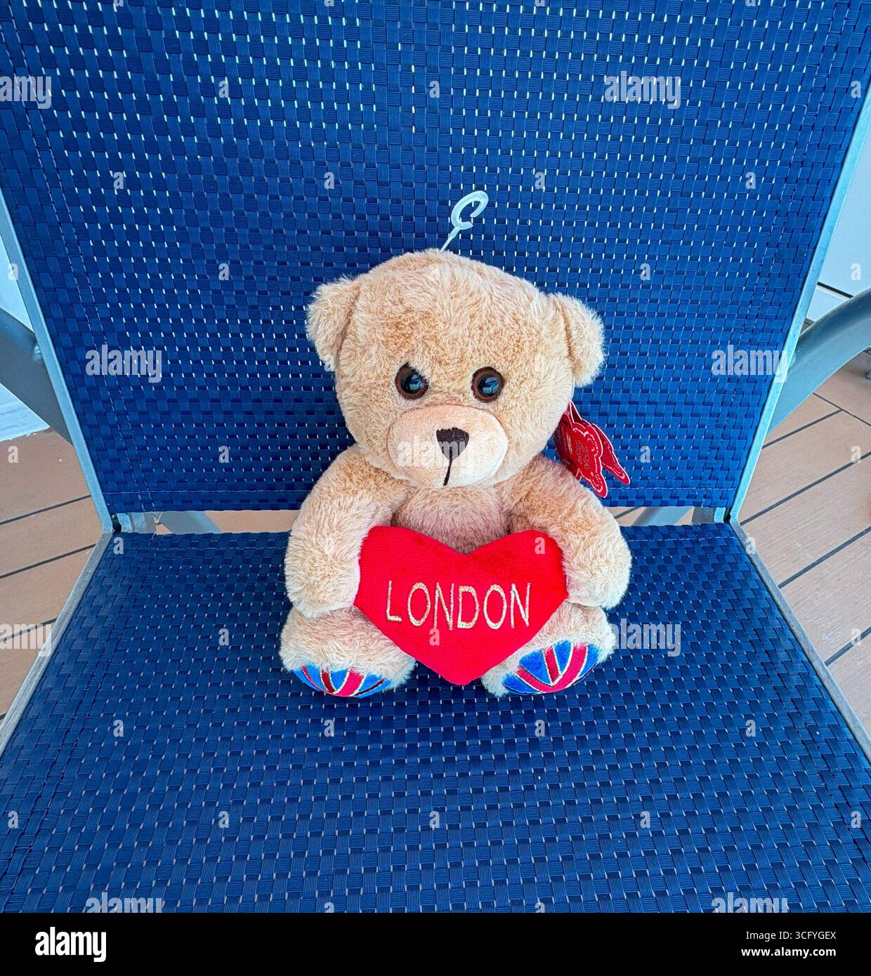 Ein Teddybär mit rotem Herz sitzt auf einem blauen Stuhl an sonniger Stelle. Stockfoto