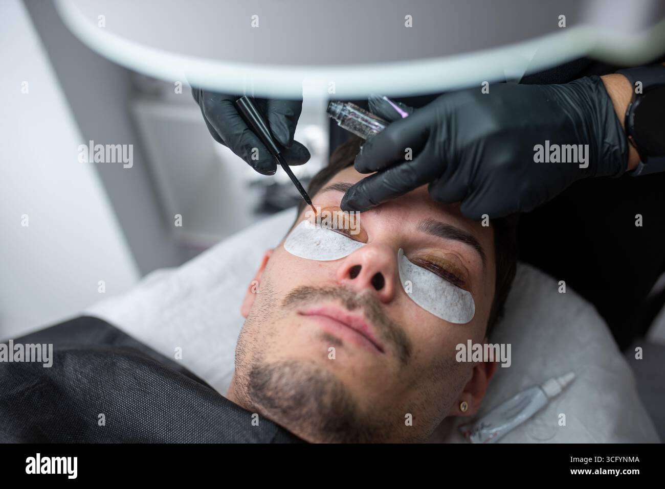Männlicher Kunde erhält Wimpernverlängerungen in einem zeitgenössischen Salon, der qualifizierte Anwendungen und professionelle Werkzeuge präsentiert Stockfoto