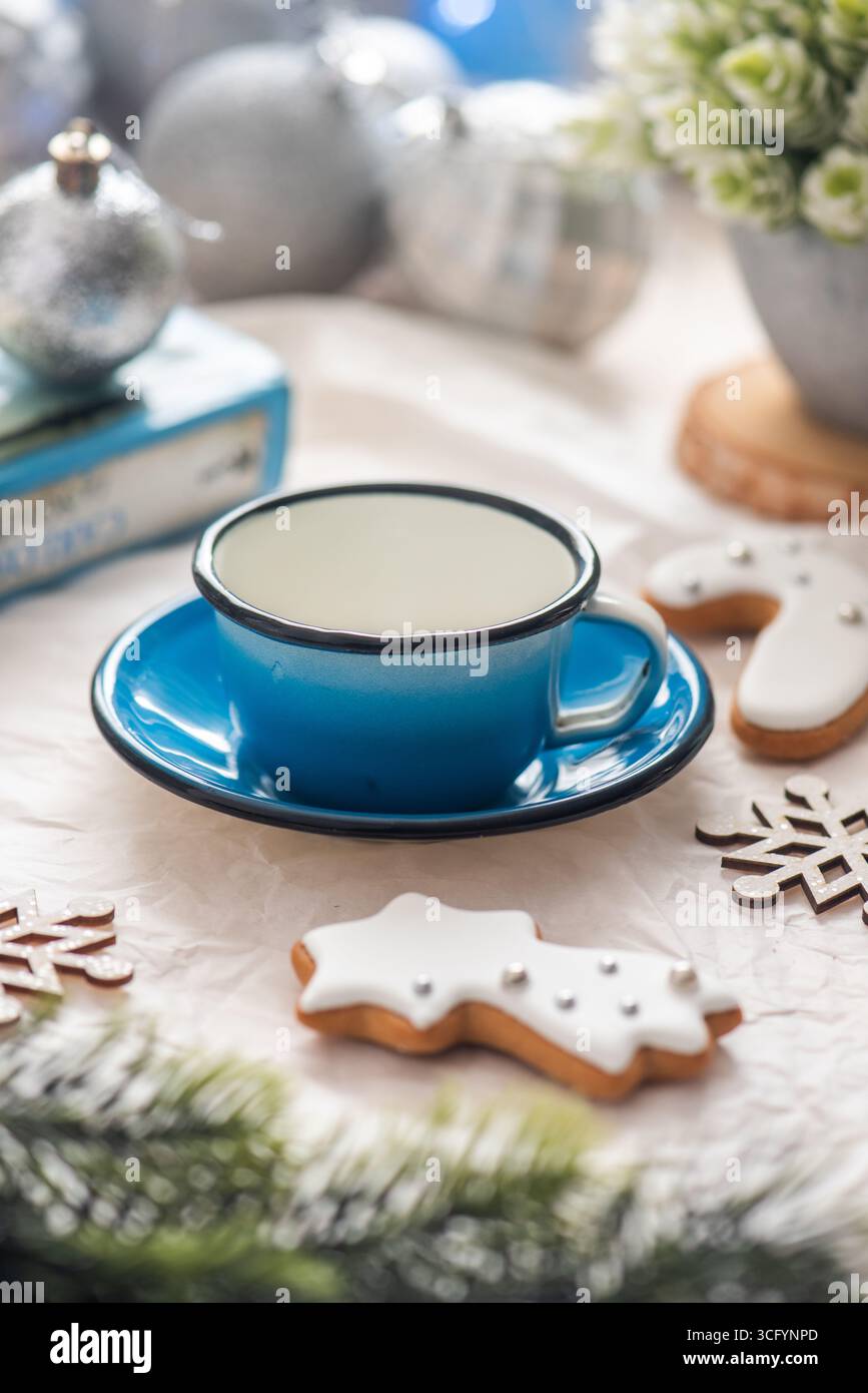 Ein blauer Keramikbecher auf einer Untertasse, umgeben von festlichen Keksen und Weihnachtsdekorationen, schafft eine warme und einladende Atmosphäre Stockfoto