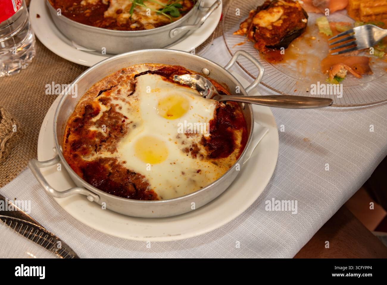 Traditionelles Shakshuka-Frühstück aus dem Nahen Osten mit pochierten Eiern, Tomatensauce und Knoblauch, serviert vom Herd in einer heißen Metallpfanne. Stockfoto