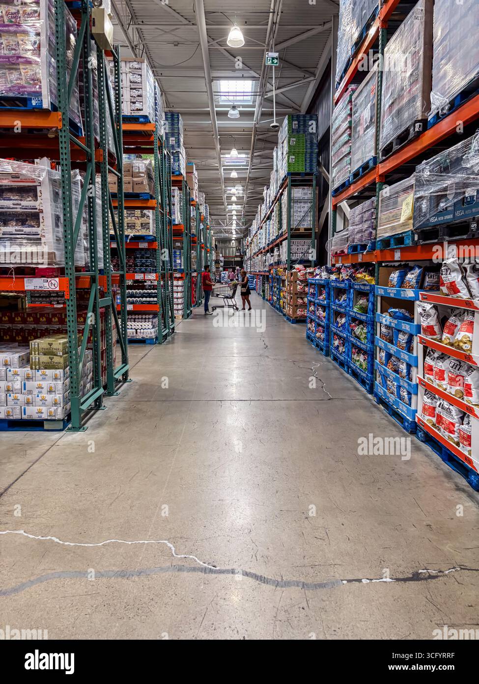 Das Innere des Costco-Lagerhauses zeigt einen langen Gang mit hohen Regalen, die mit Massenprodukten bestückt sind. Käufer können sehen, wie sie ihre Wagen schieben. Stockfoto