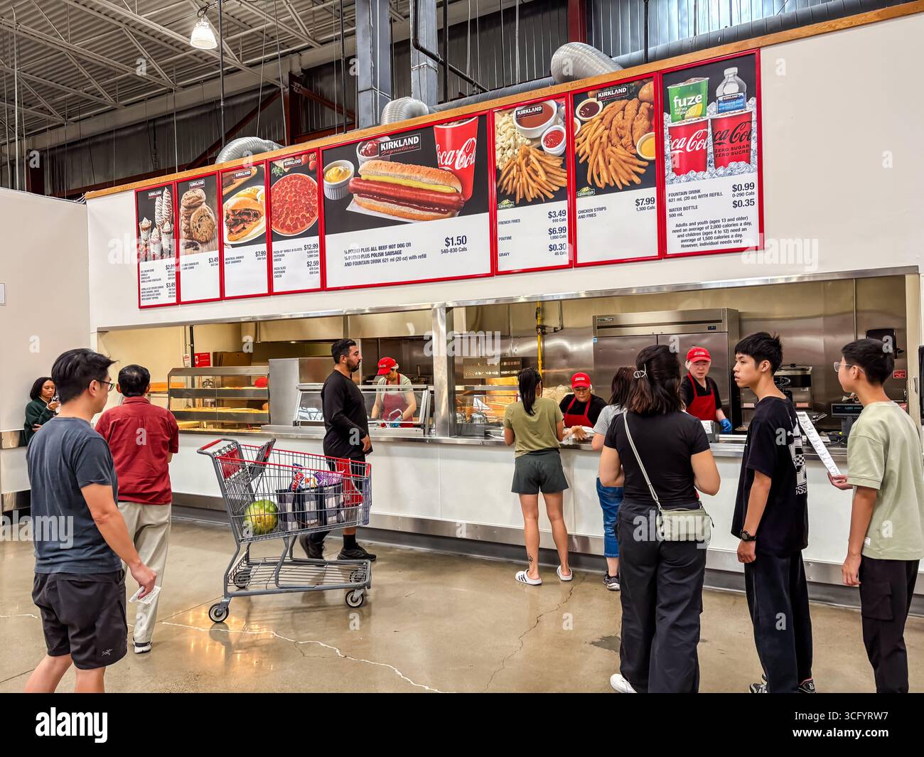 Das Innere des Costco Food Courts zeigt verschiedene Kunden, die sich anstellen, um preisgünstiges Fast Food von der Speisekarte zu bestellen, einschließlich Hot Dogs und Pizza. Stockfoto