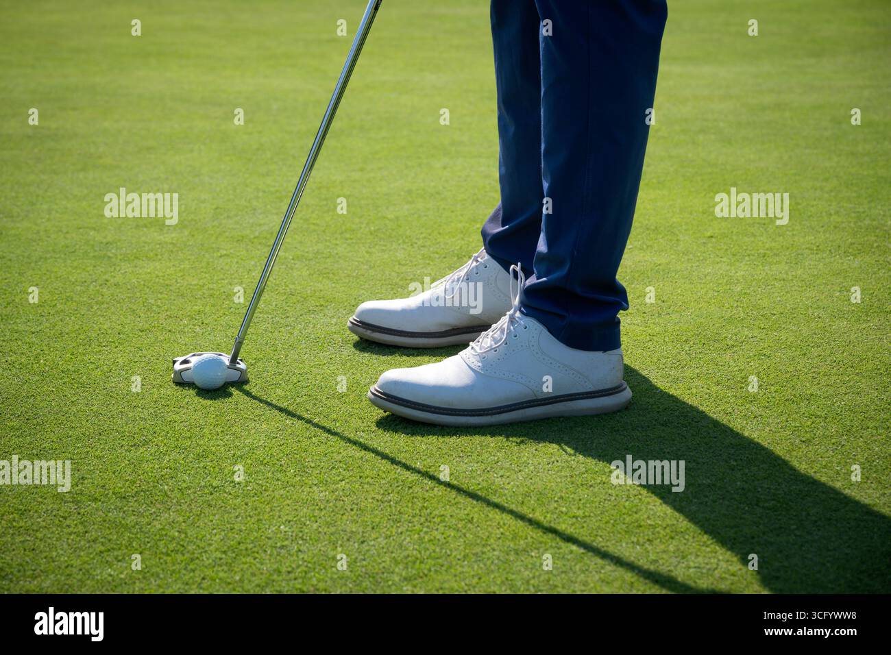 Der Golfspieler bereitet sich darauf vor, den Ball auf einem sonnigen Grün zu schlagen, wobei er sich auf die Füße und den Schläger konzentriert Stockfoto